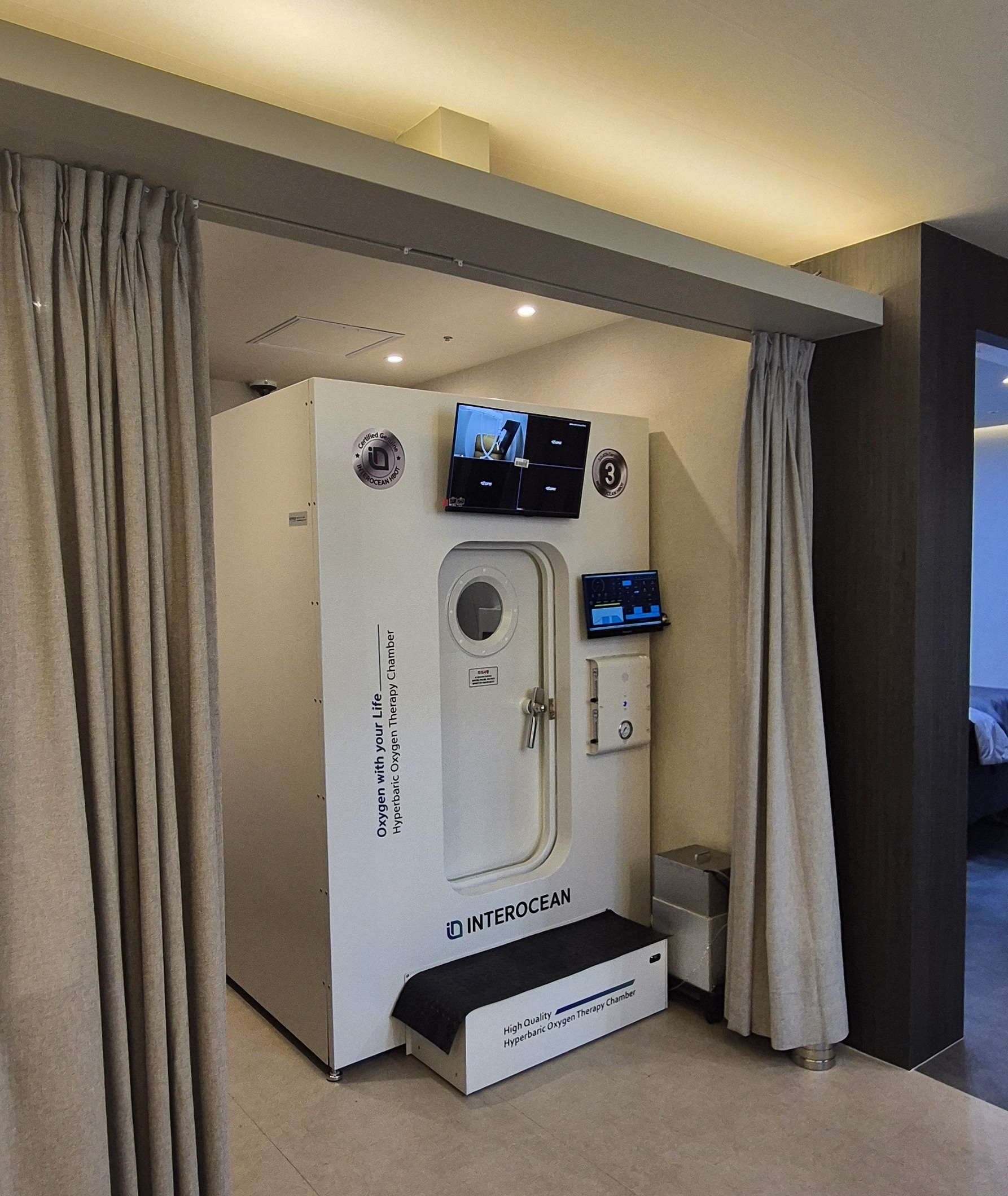 Interior view of a medical-grade hyperbaric oxygen therapy chamber with a patient breathing through a 100% oxygen mask.