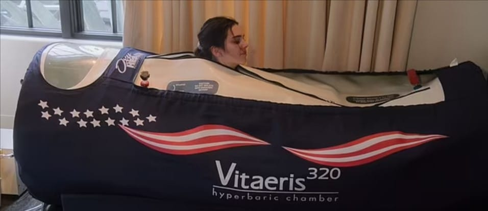 Interior view of a medical-grade hyperbaric oxygen therapy chamber with a patient breathing through a 100% oxygen mask.